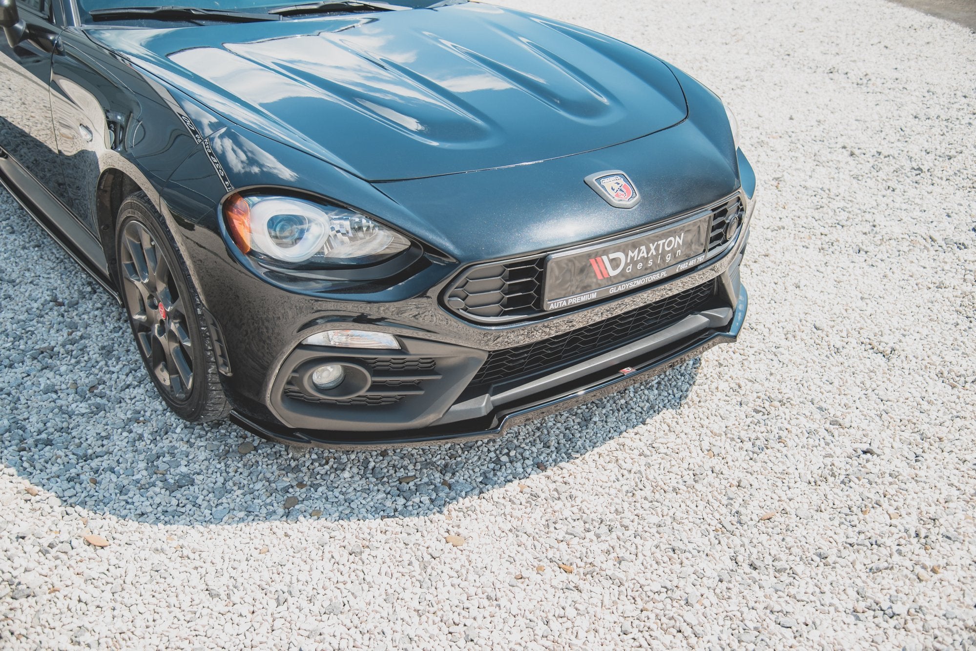 Front splitter på Abarth 124 Spider med sort Maxton Design, tydelig grill og markerte panserlinjer på grus.