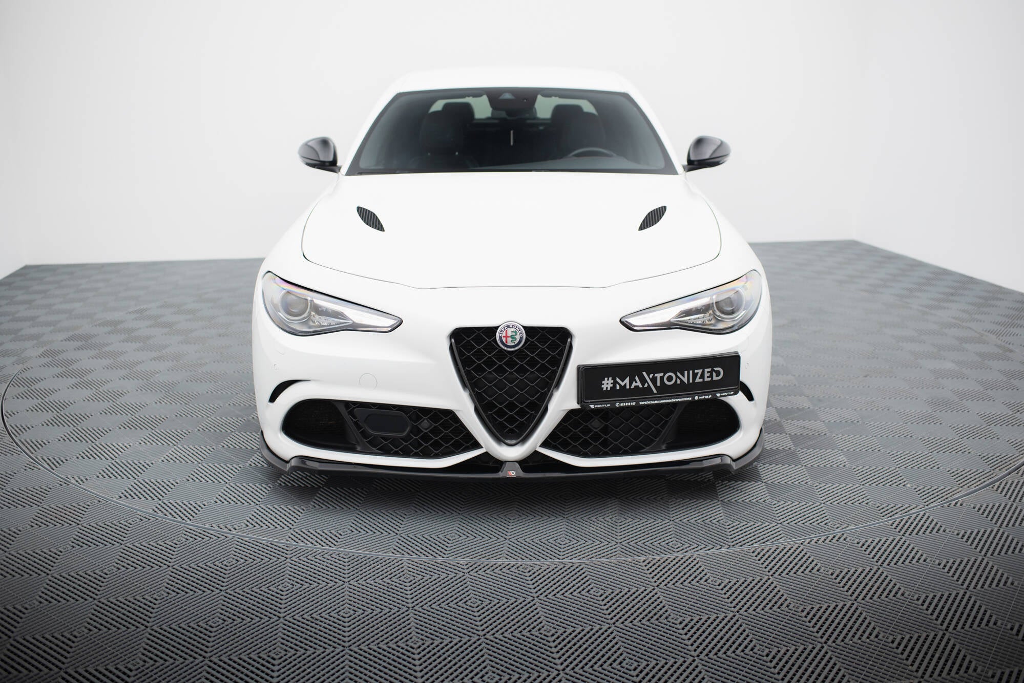 Frontleppe på Alfa Romeo Giulia Quadrifoglio, hvit bil sett forfra med svart grill på rutete gulv.