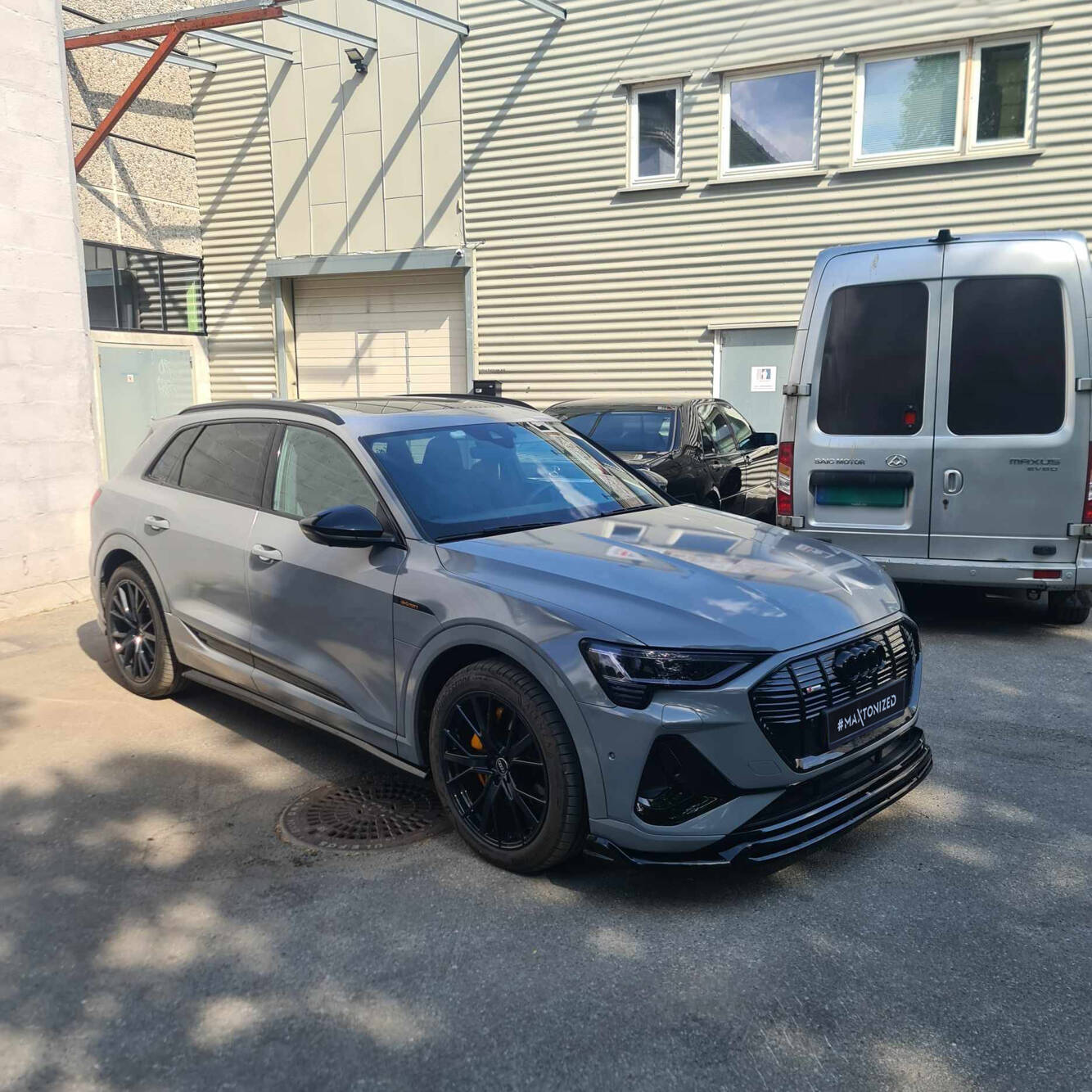 Spoiler på Audi E-Tron S-Line SUV med sorte detaljer og gule bremsekalipere parkert foran industribygg.