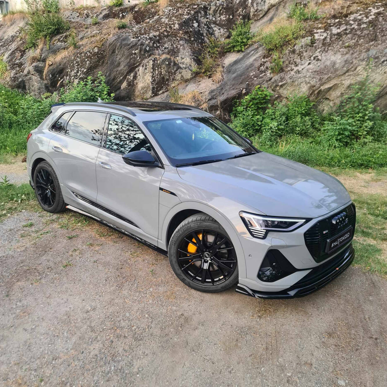 Front lip på Audi E-Tron S-Line, grå SUV med sorte felger og oransje bremsekalipere utendørs.