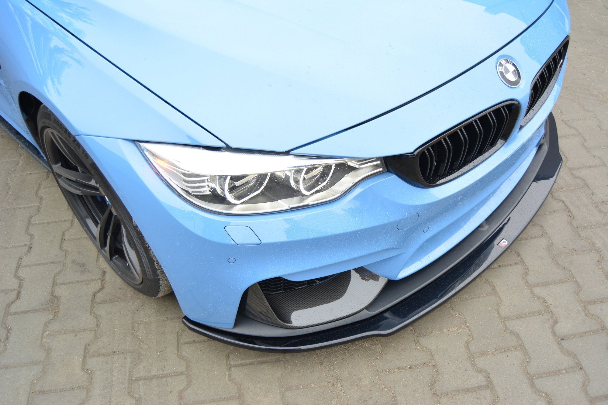 Front splitter på BMW M4 F82 med karbonfiber, synlig sort grill og frontlys, parkert på belegningsstein.