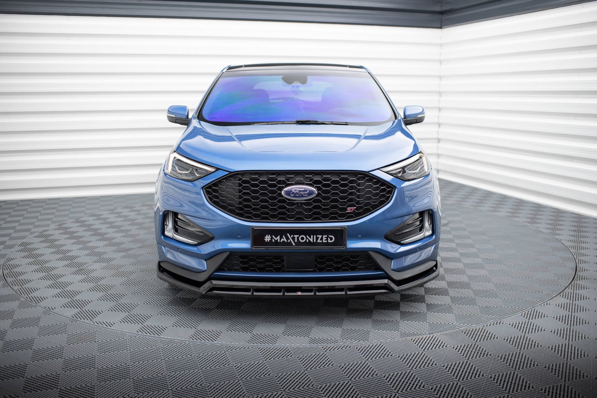 Frontleppe på blå Ford Edge St MK2, sett forfra med svart grill og LED-frontlykter i lyst showroom.