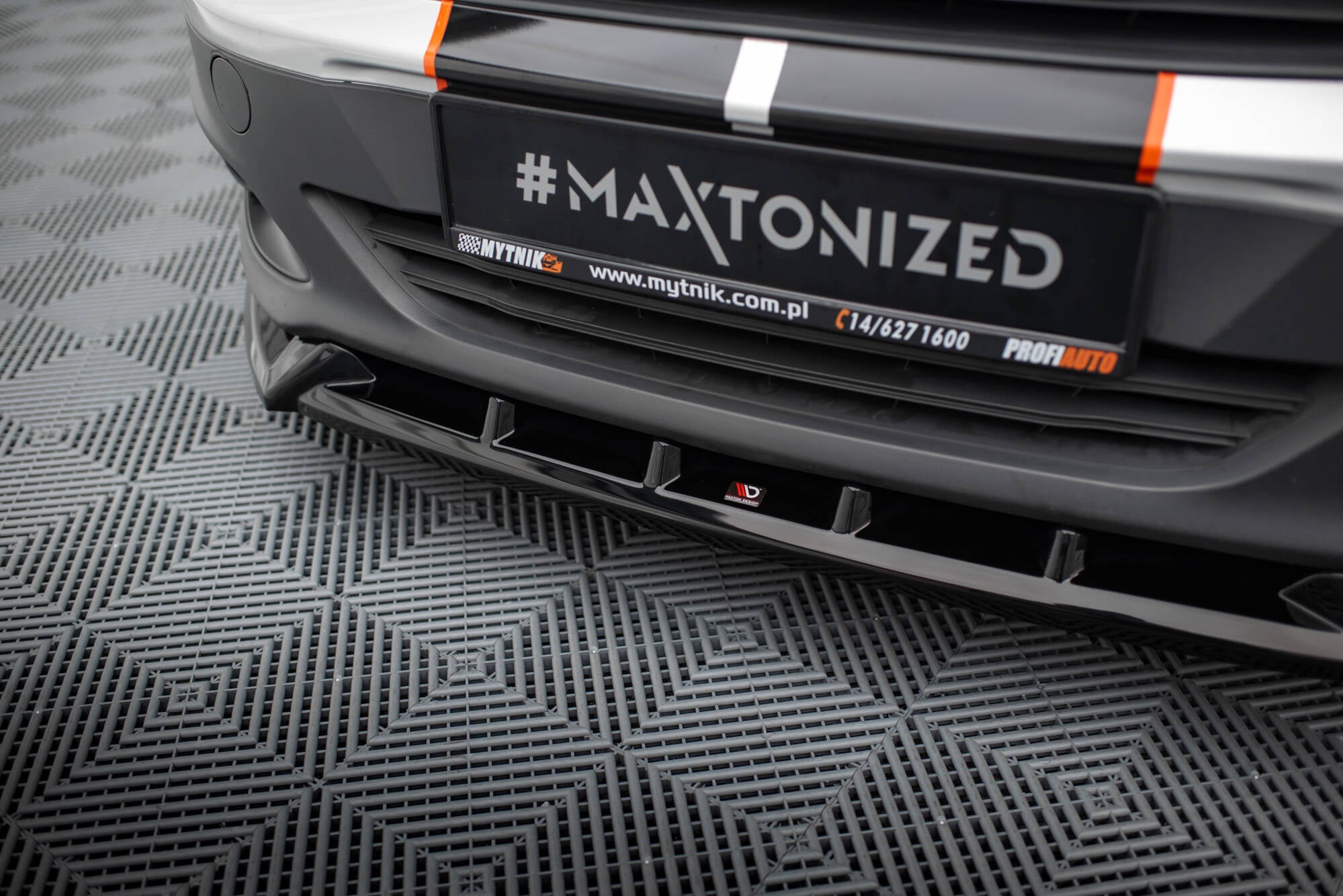 Spoiler til Ford Transit Courier MK1 i sort blank plast montert foran, sett fra lav vinkel med gulvmønster.