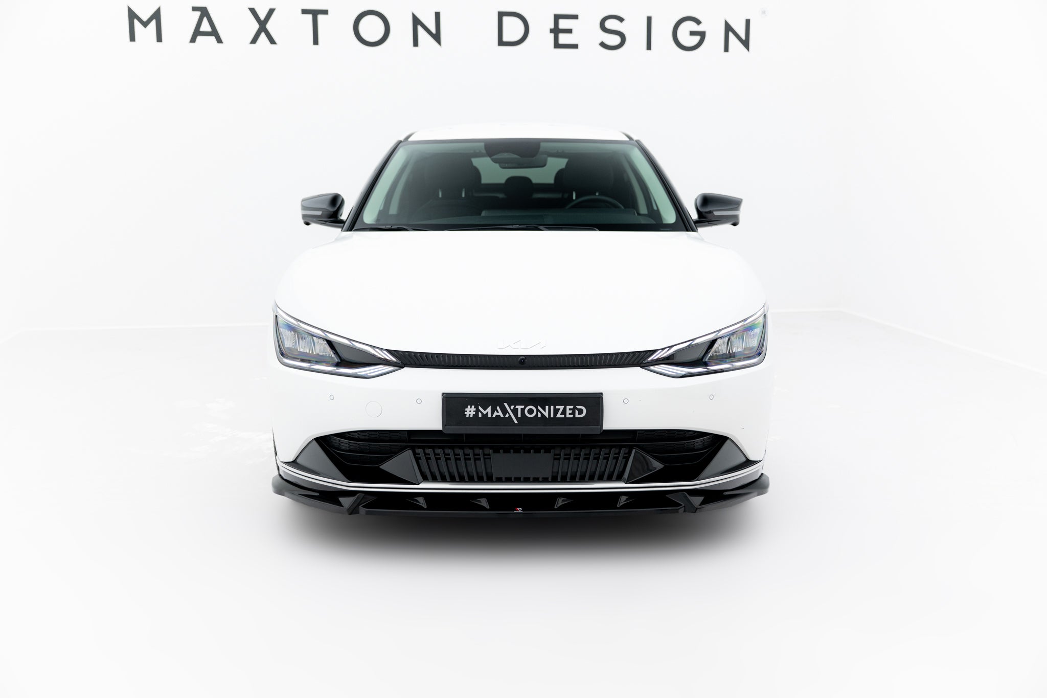 Frontleppe på hvit Kia Ev6 MK1 med sorte detaljer, sett forfra i lyst, minimalistisk rom.