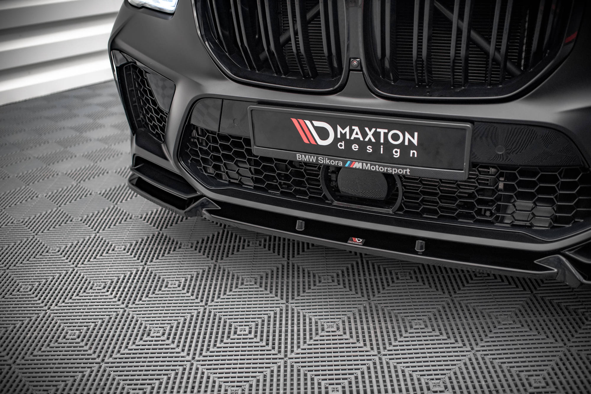 Spoiler BMW X5M F95 V.1 i sort blank plast med rutenettmønstret grill og Maxton Design-logo.