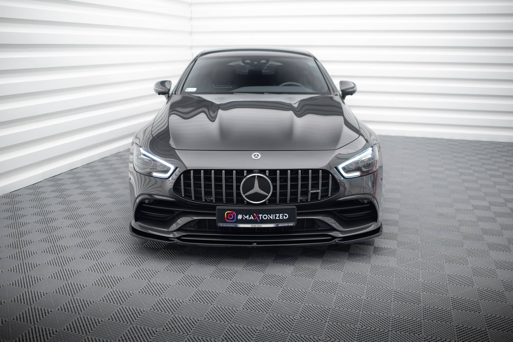 Frontleppe på Mercedes GT 53 4-Dør Coupe V.1 sett forfra med grill og frontlykter i lyst rom.