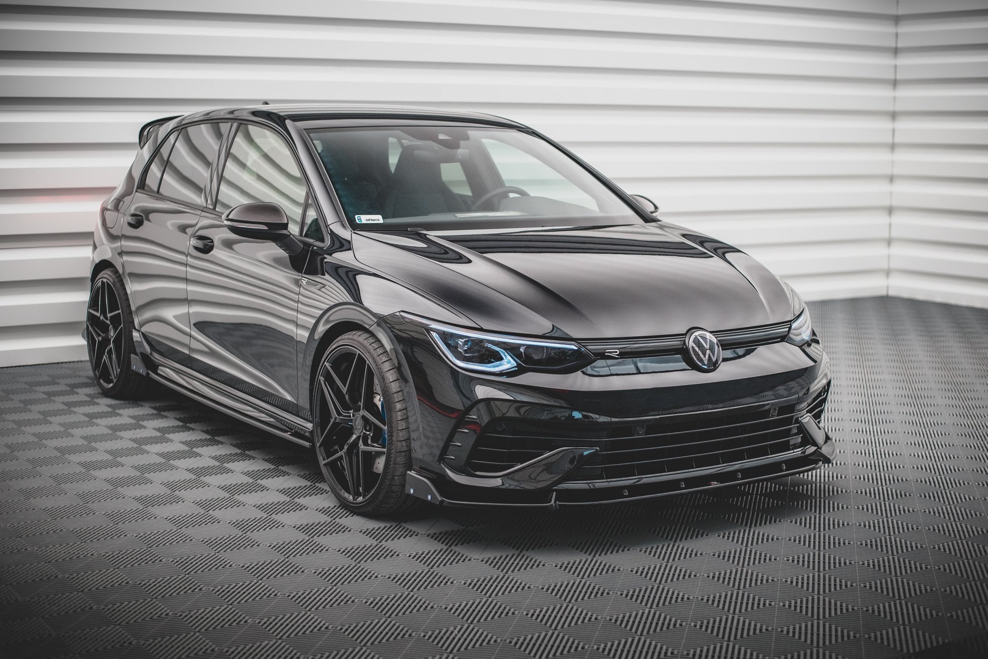 Spoiler på VW Golf R MK8 V.2, sort bil med svarte felger, sett forfra i innendørs miljø.