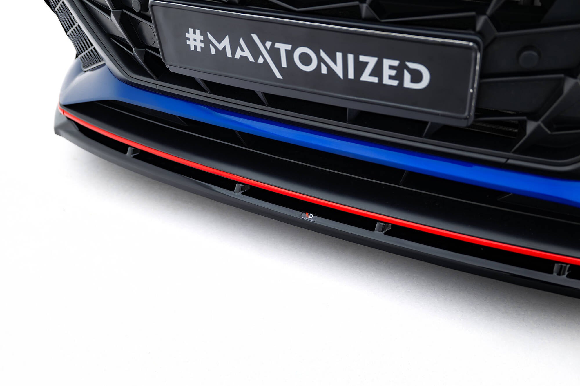 Spoiler til Hyundai Elantra N MK7 V.2, sort plast med rød stripe og blå detalj, sett forfra mot hvit bakgrunn.