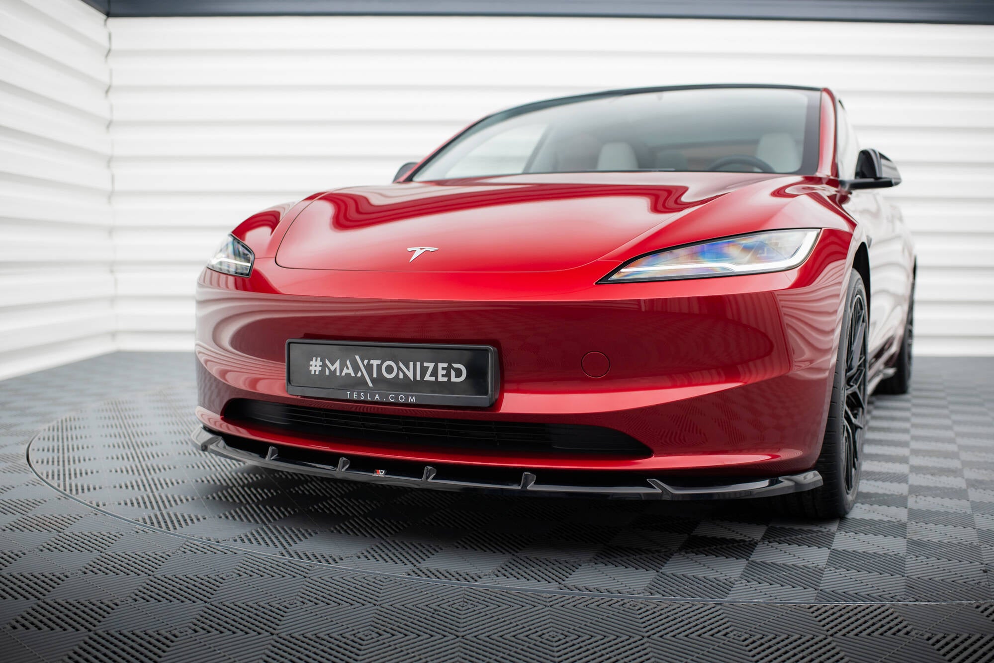 Frontspoiler på rød Tesla Model 3 Project Highland V.2 med svarte detaljer sett forfra innendørs.