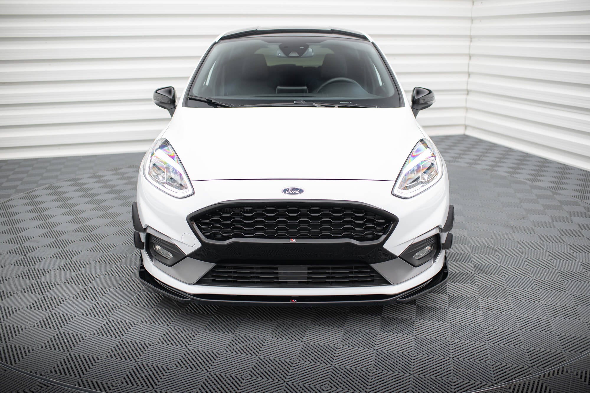 Frontleppe på Ford Fiesta MK8 ST med sorte detaljer, frontlykter og speil, fotografert innendørs.