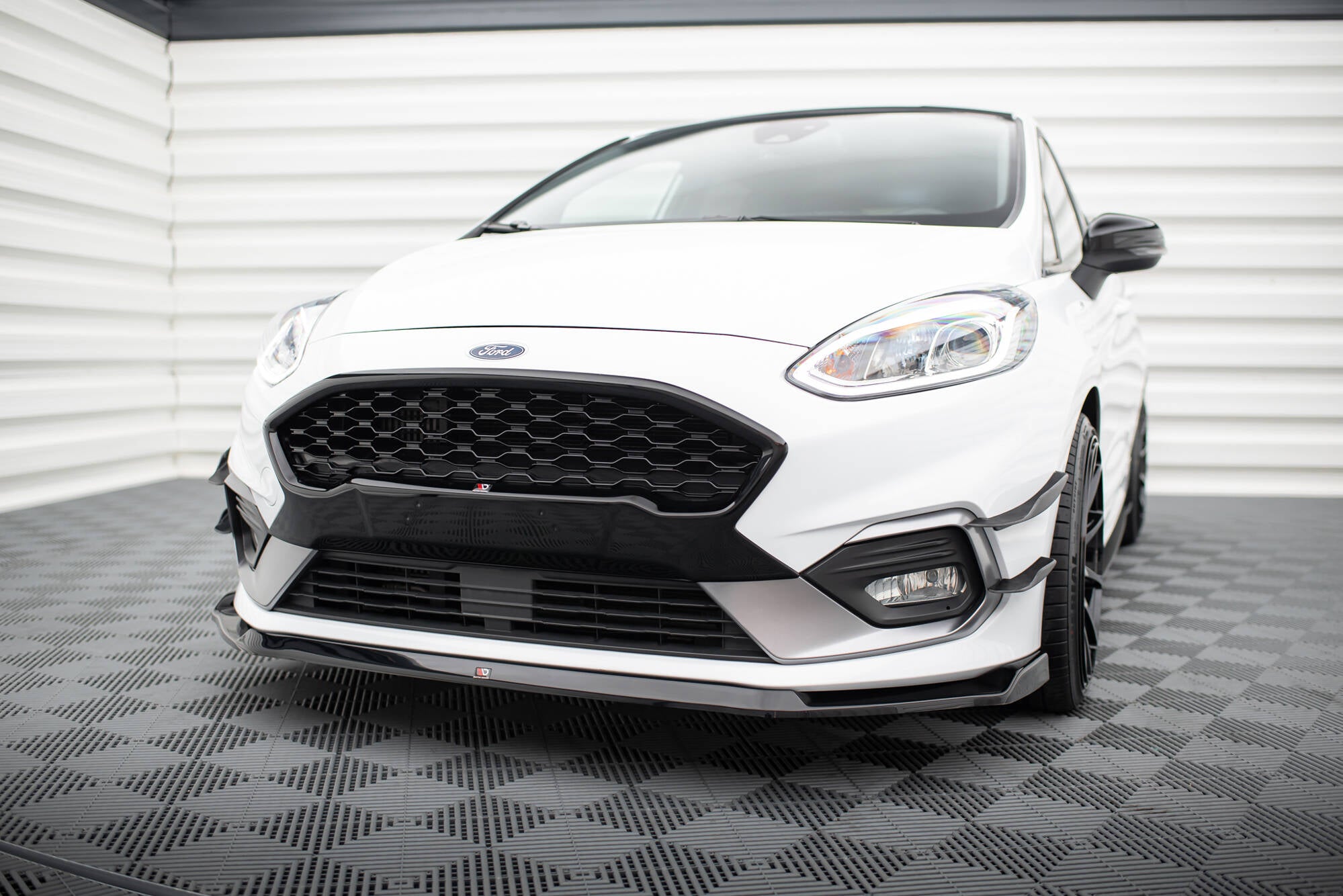 Frontspoiler Ford Fiesta MK8 St montert på hvit bil med sort grill og LED-frontlykter, innendørs.