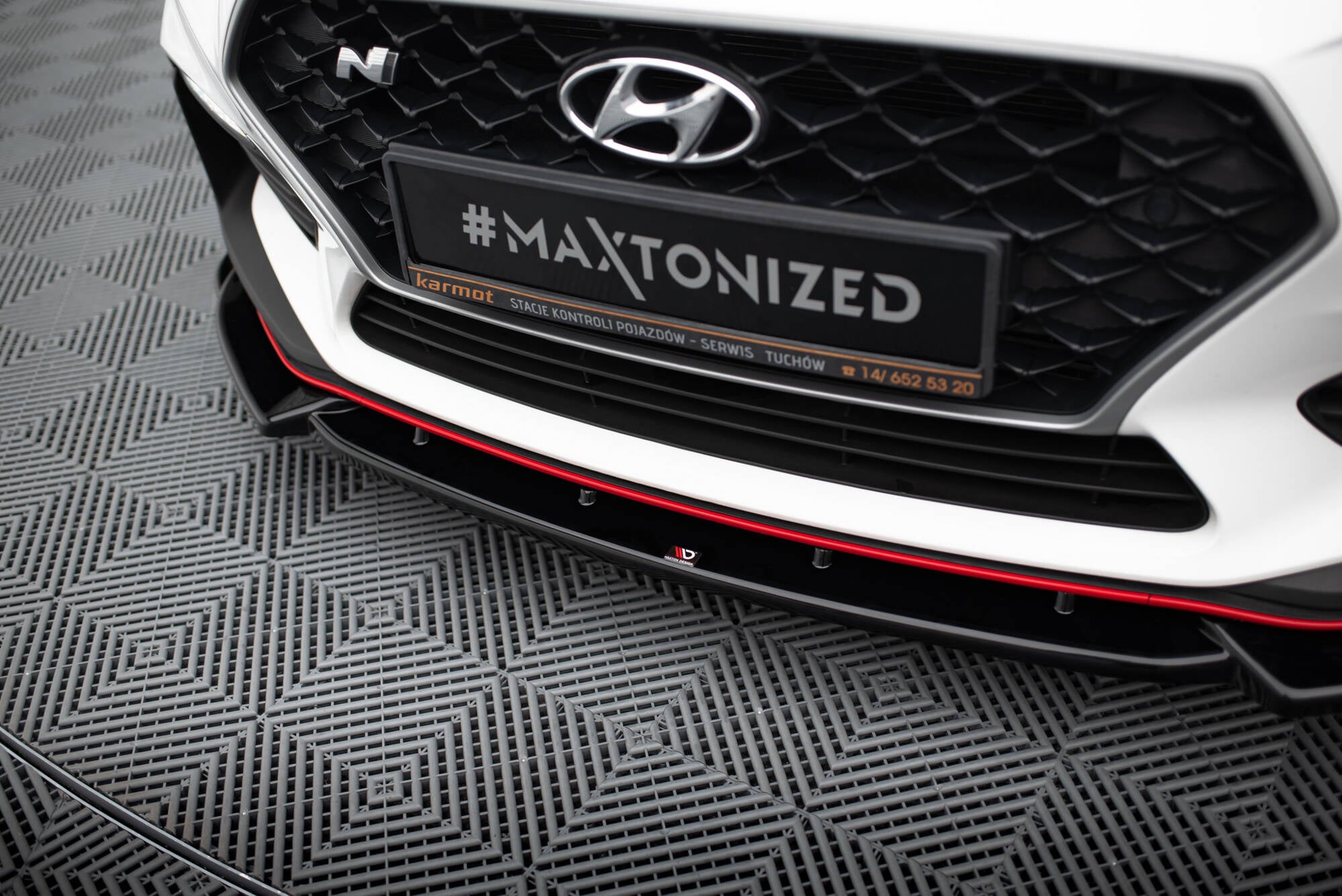 Spoiler til Hyundai I30 N MK3 i svart plast med rød stripe, montert under hvit frontfanger.