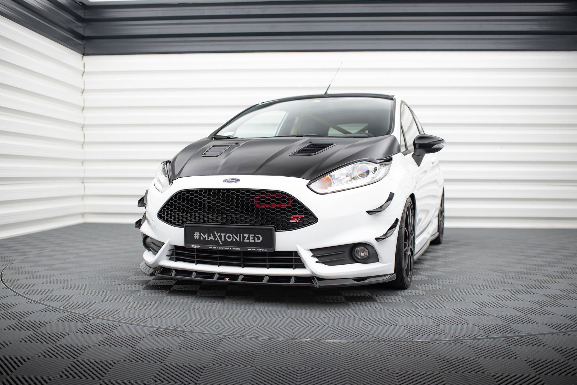Frontspoiler Ford Fiesta St MK7 Facelift V.6 på hvit bil med matt svart panser i lyst industrilokale.