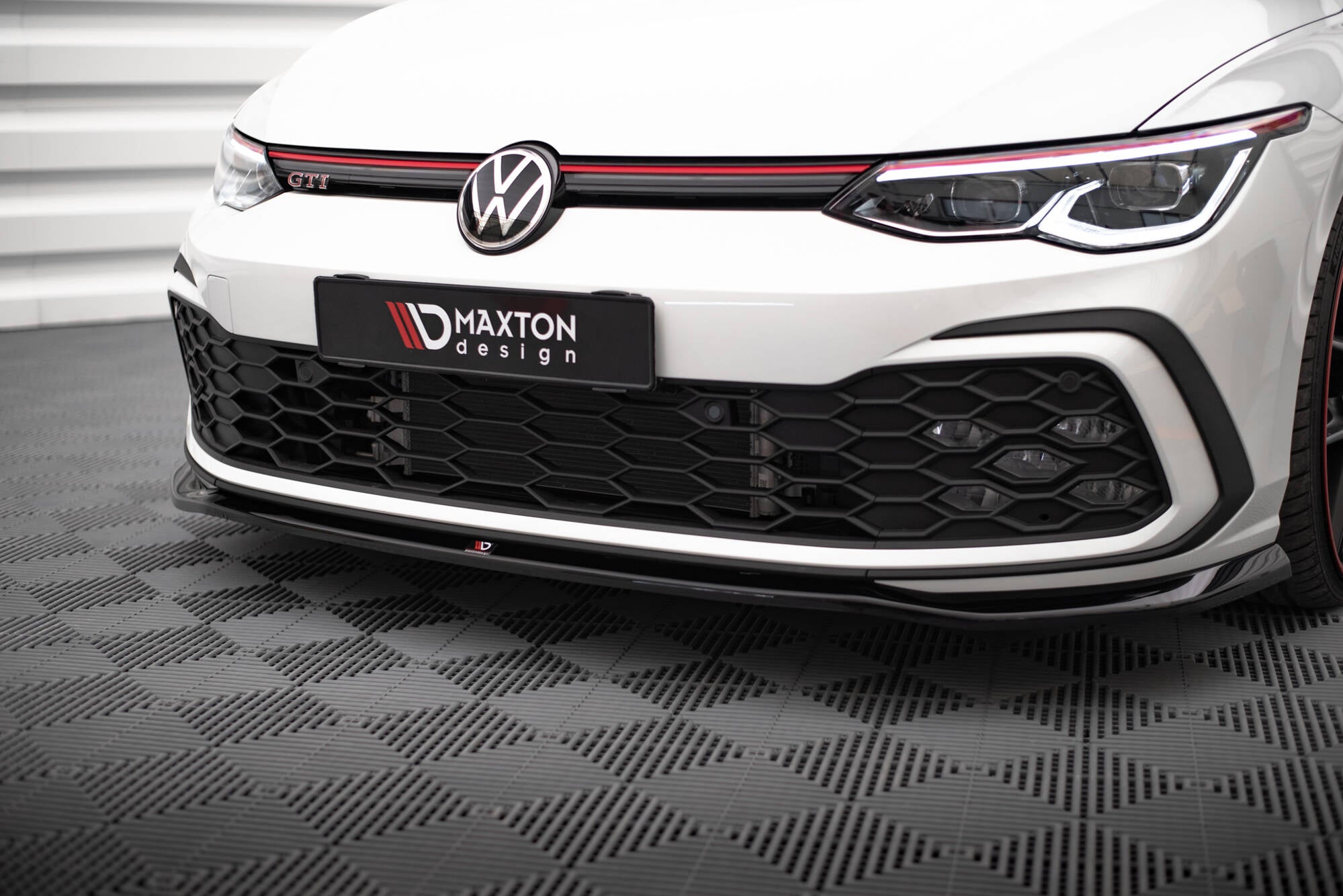 Frontspoiler VW Golf GTI MK8 V.7 montert på hvit bil med sort grill og røde detaljer, sett fra lav vinkel.