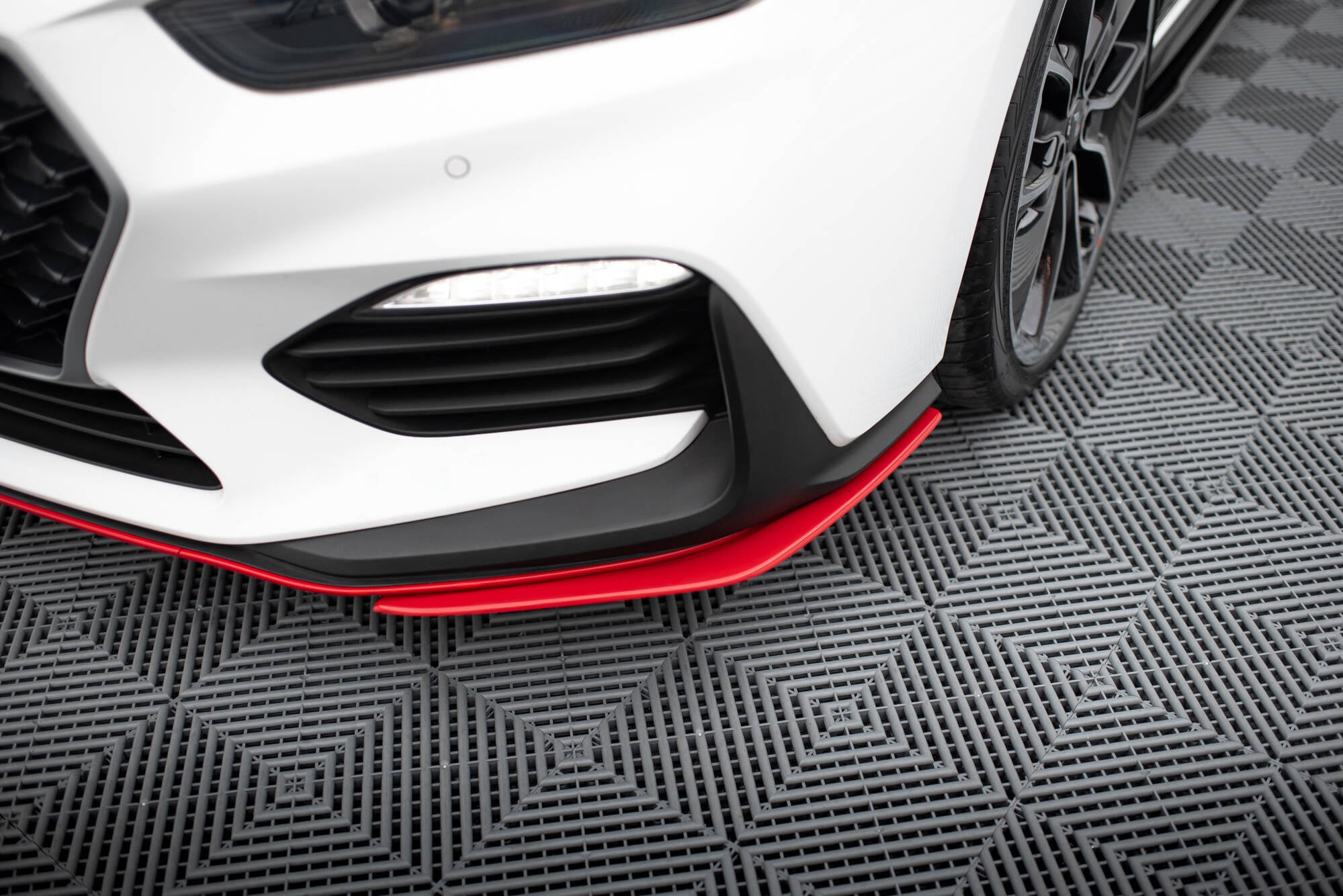 Front splitter på Hyundai I30 N MK3, nærbilde av rød splitter mot hvit front og svart grill.