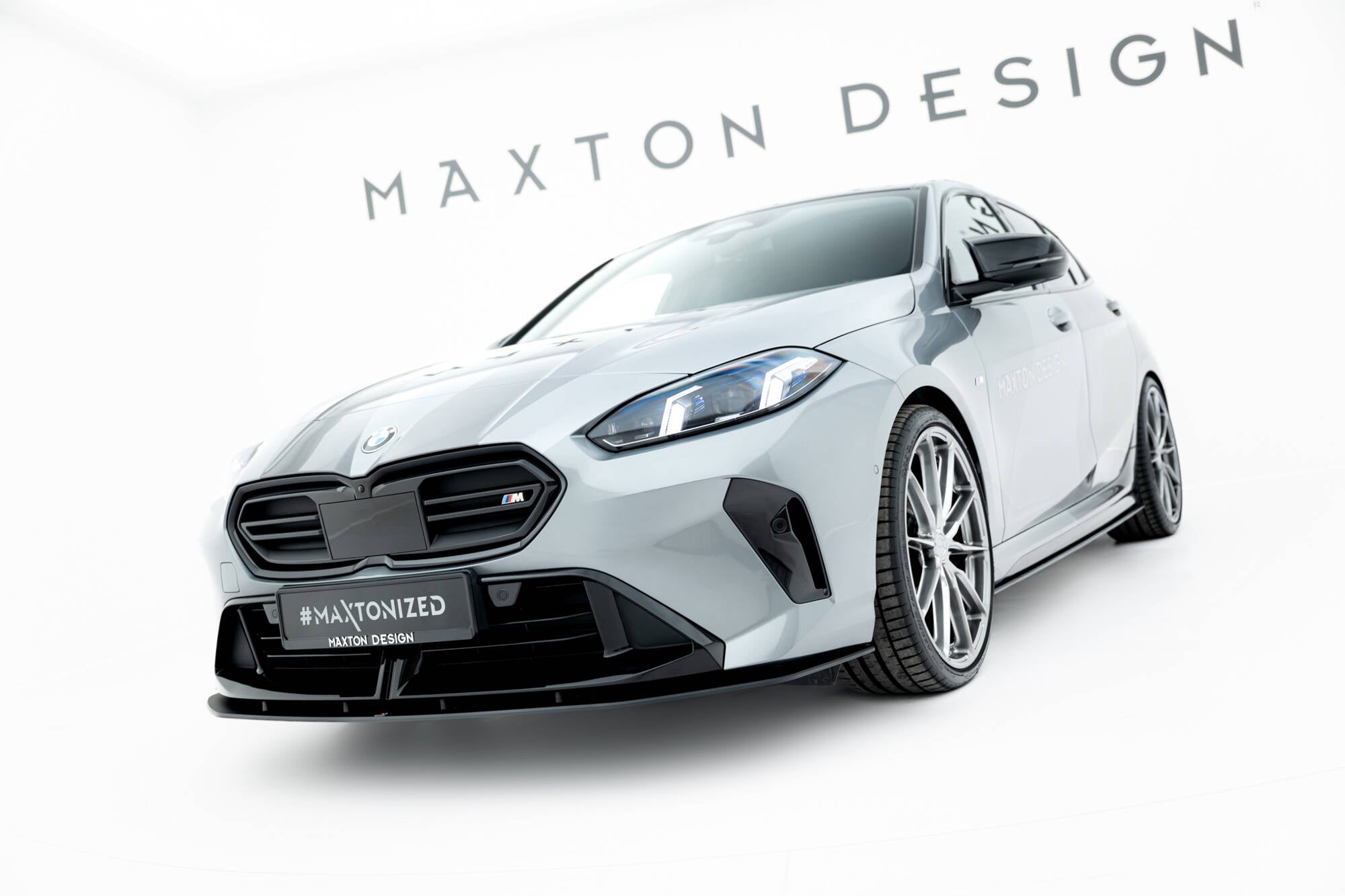 Frontspoiler BMW F70 M135I Front V1 montert på lysegrå sportsbil med svarte detaljer og store sølvfelger.