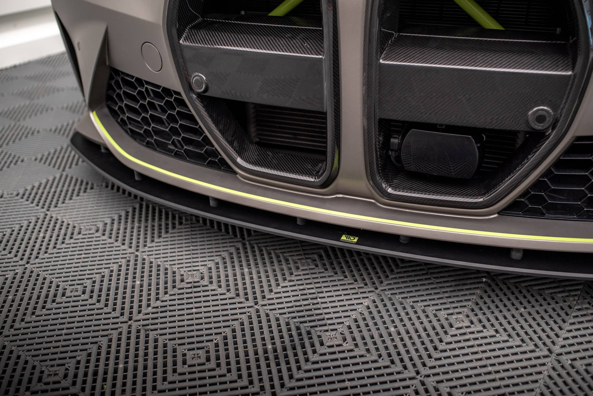 Front splitter på BMW M4 G82 med karbonfiber, sorte og lysegule detaljer, synlig grill og matt overflate.