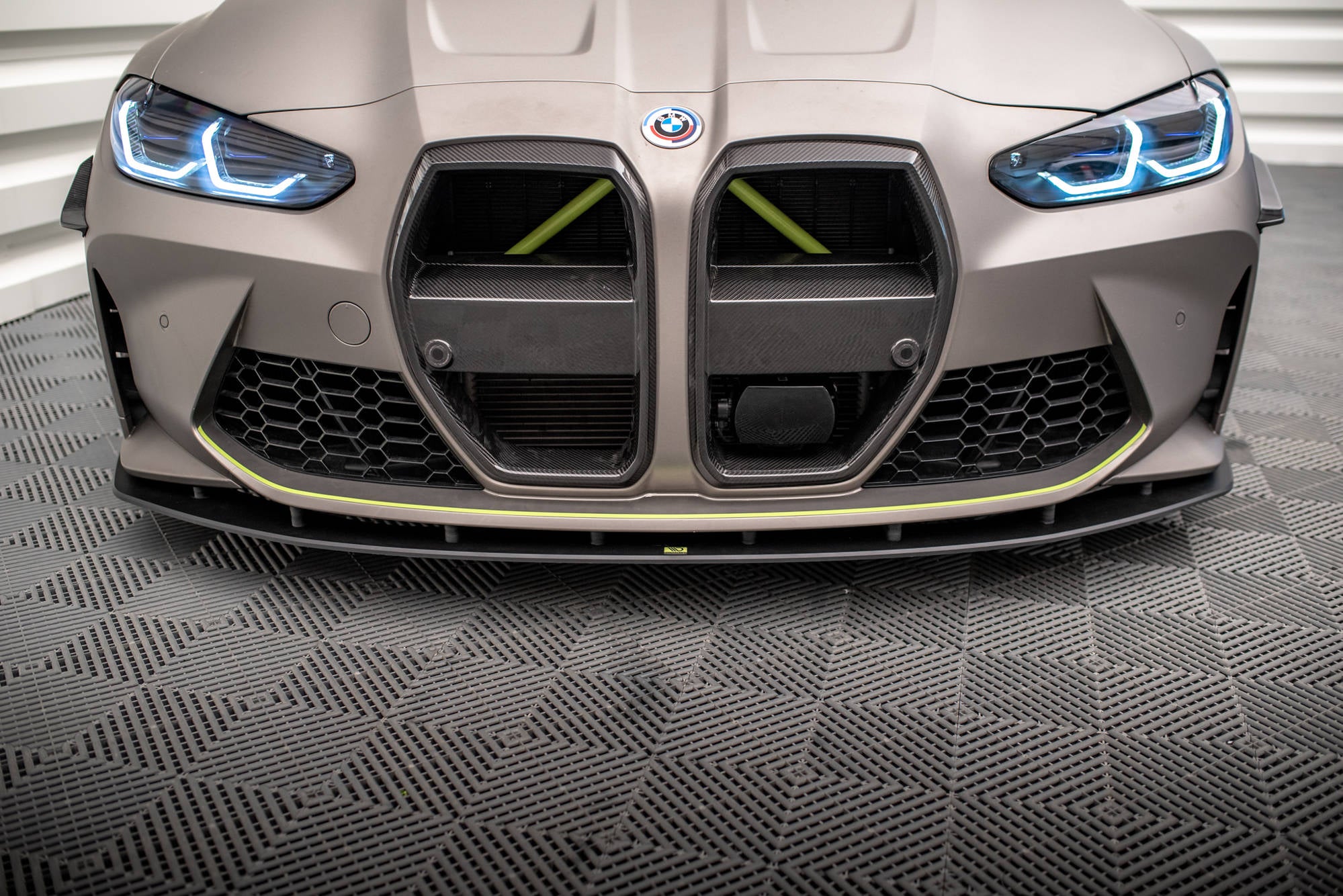 Spoiler på BMW M4 G82 med matt grå finish, karbonfiber-detaljer og blå LED-lys sett forfra.