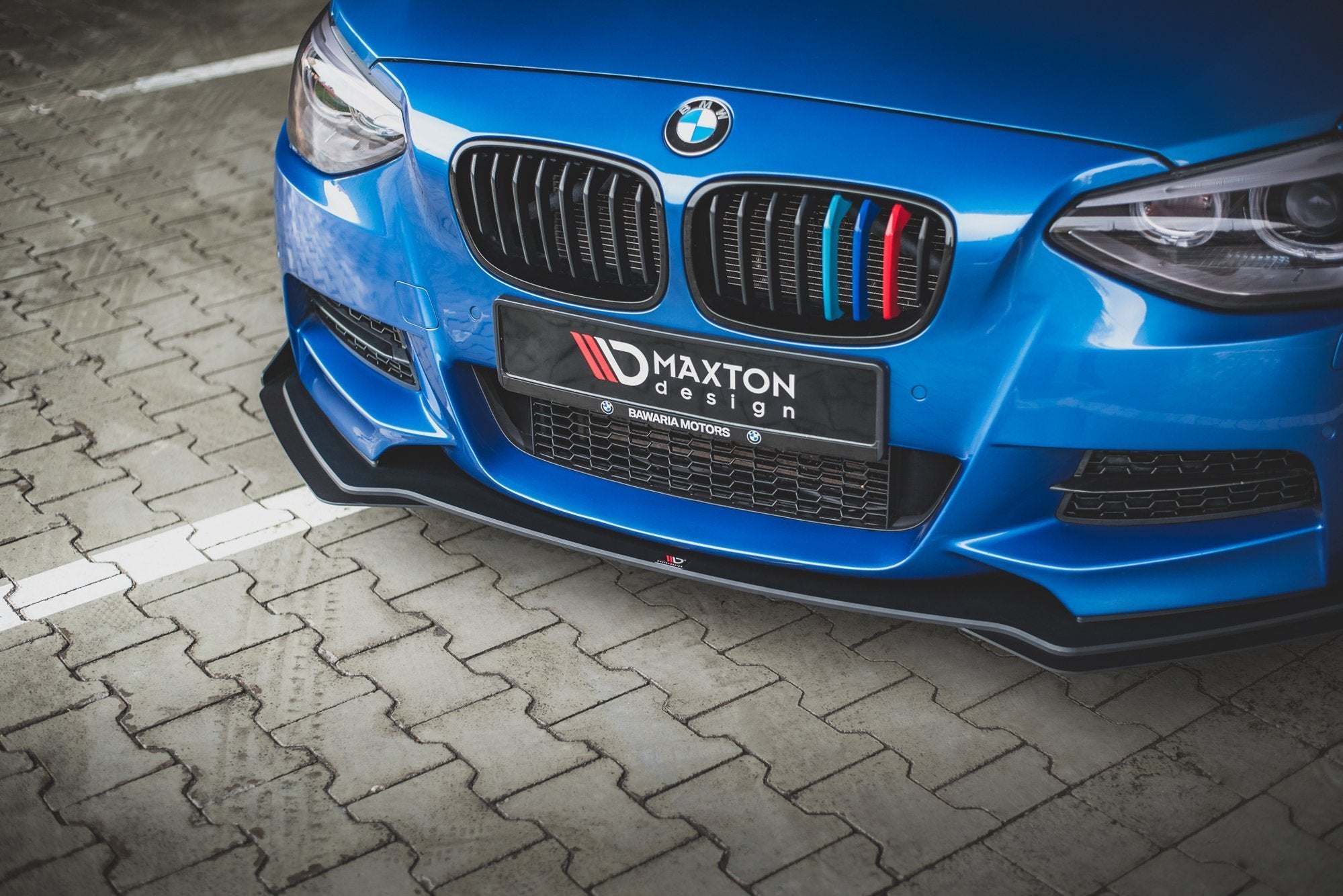 Frontleppe på BMW M135I F20 2011 med svart splitter og fargede grilldetaljer, sett i halvprofil.