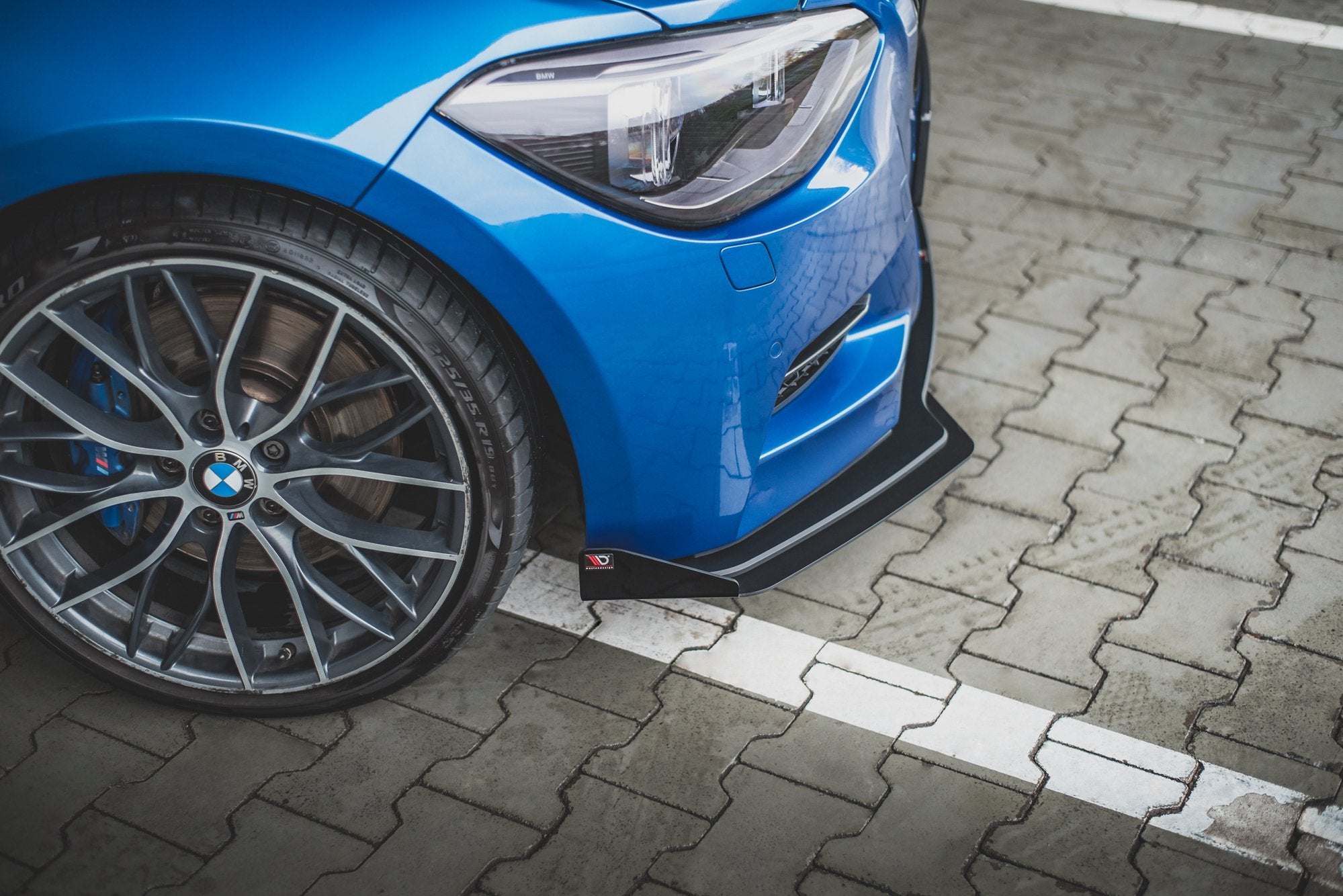 Front splitter på blå BMW M135I F20 med sølvfelg og synlig frontlykt, parkert utendørs.