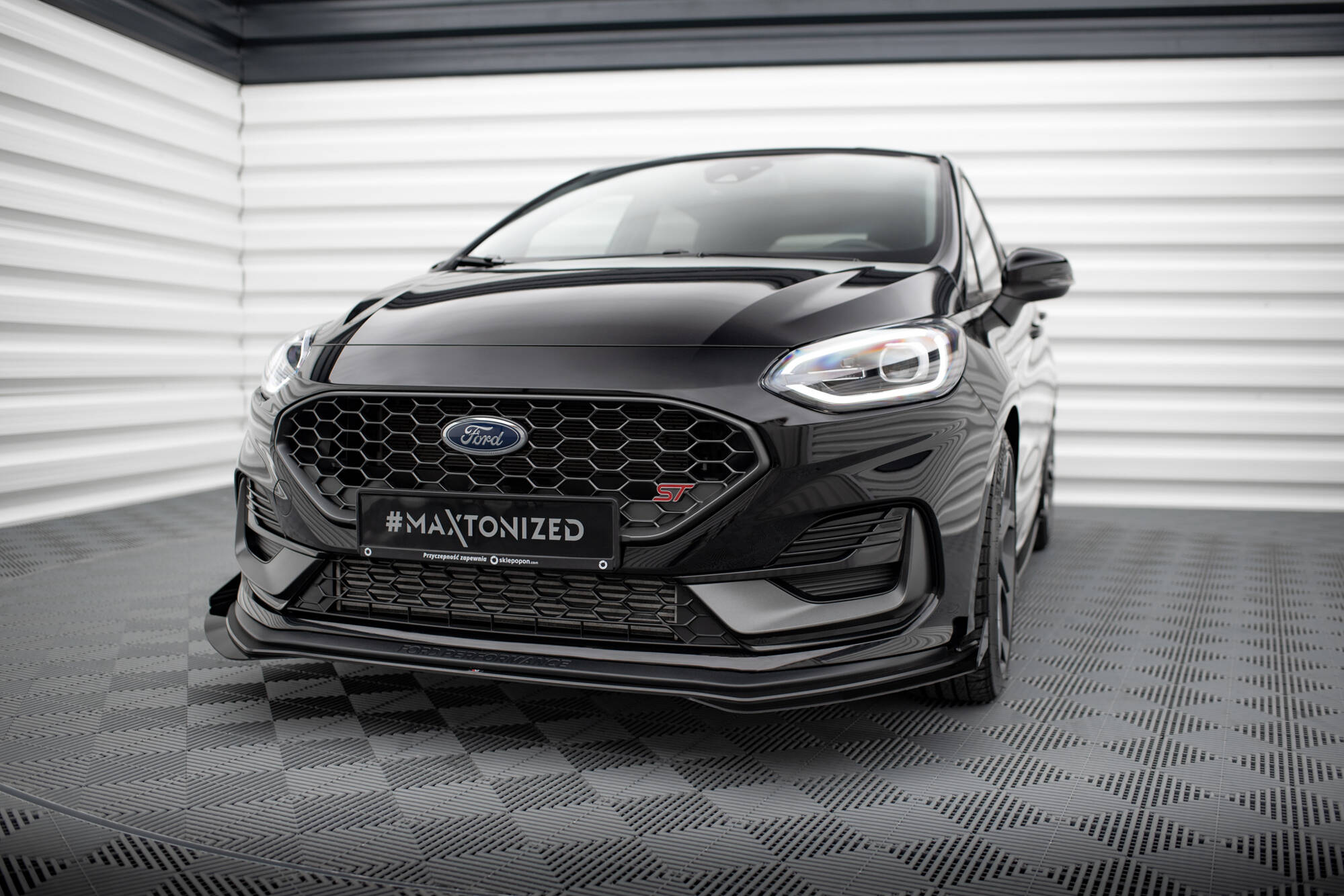 Frontspoiler på Ford Fiesta St MK8 Facelift med flaps, sett forfra i lyst rom med mønstrede gulvplater.