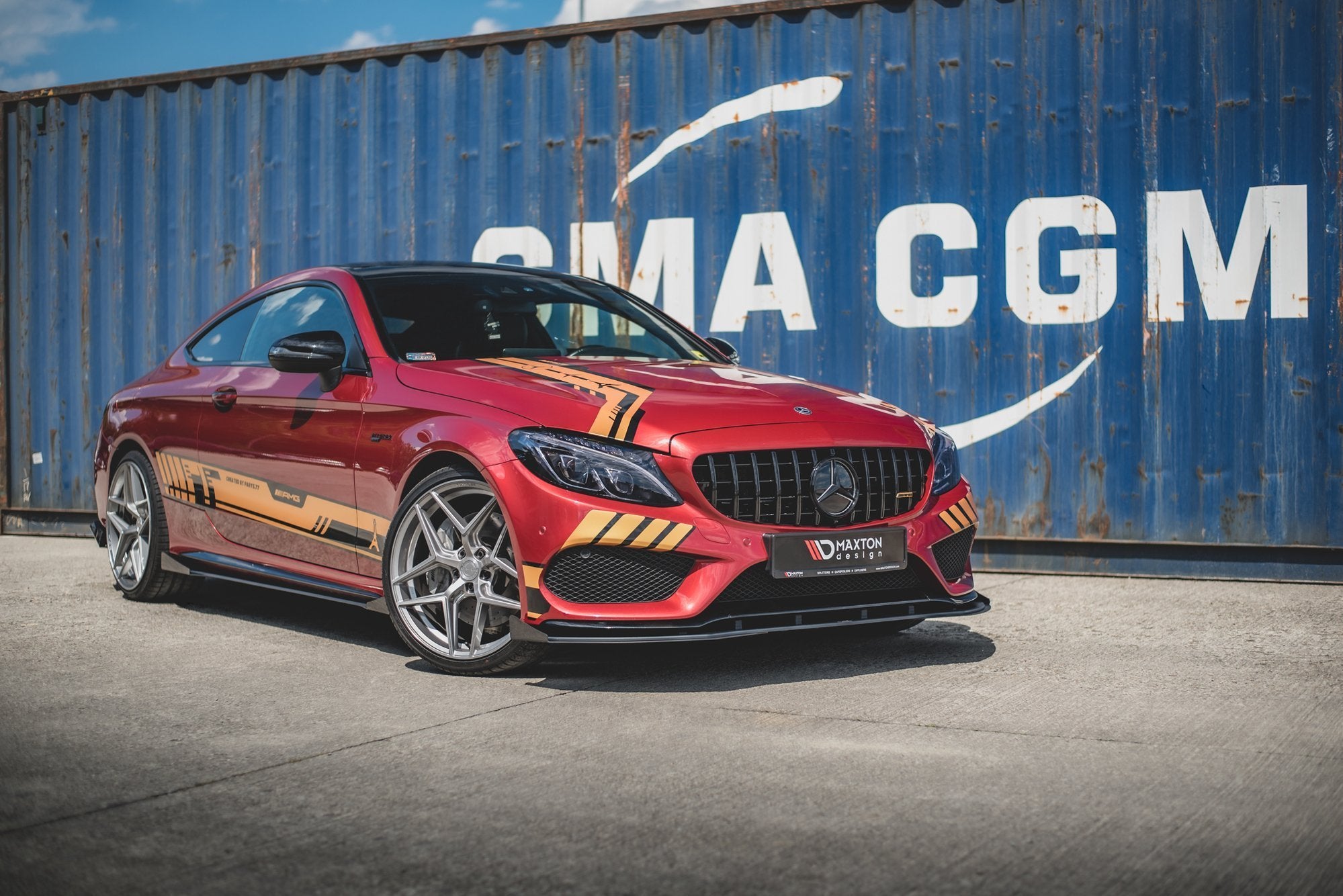 Frontleppe på Mercedes C43 Coupe C205 med sorte og gule striper, sett skrått forfra foran blå container.