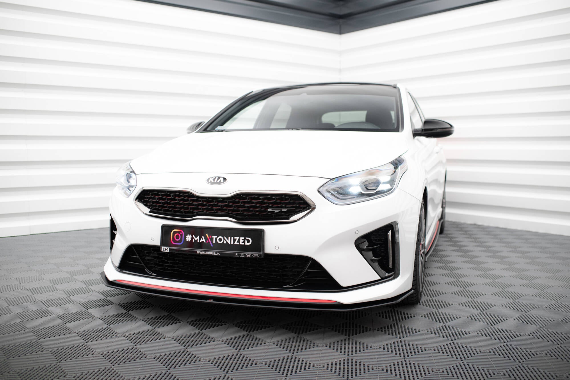 Frontspoiler til Kia Ceed GT MK3 med rød stripe, sett på hvit bil med LED-lys i lyst rom.