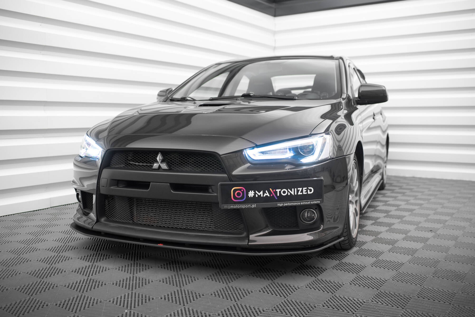 Frontspoiler Mitsubishi Lancer Evo X V1 montert på svart sportsbil med LED-lys, fotografert innendørs.
