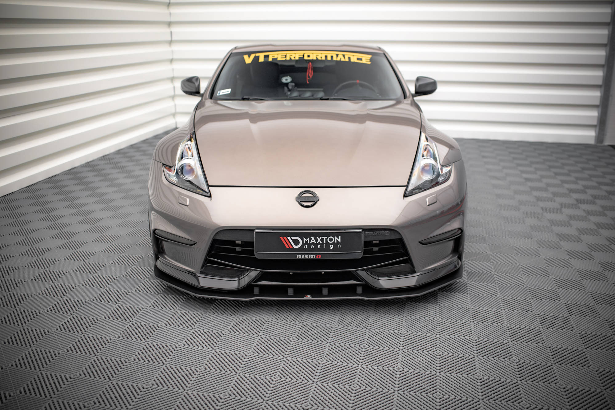 Frontleppe på Nissan 370Z Nismo Facelift sølvfarget sportsbil med sort splitter, sett forfra i lyst rom.