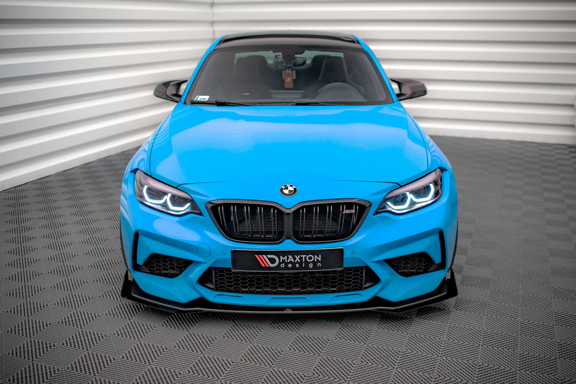 Frontspoiler BMW M2 Competition F87 V.1 på blå sportsbil sett forfra med LED-lykter og sort grill.