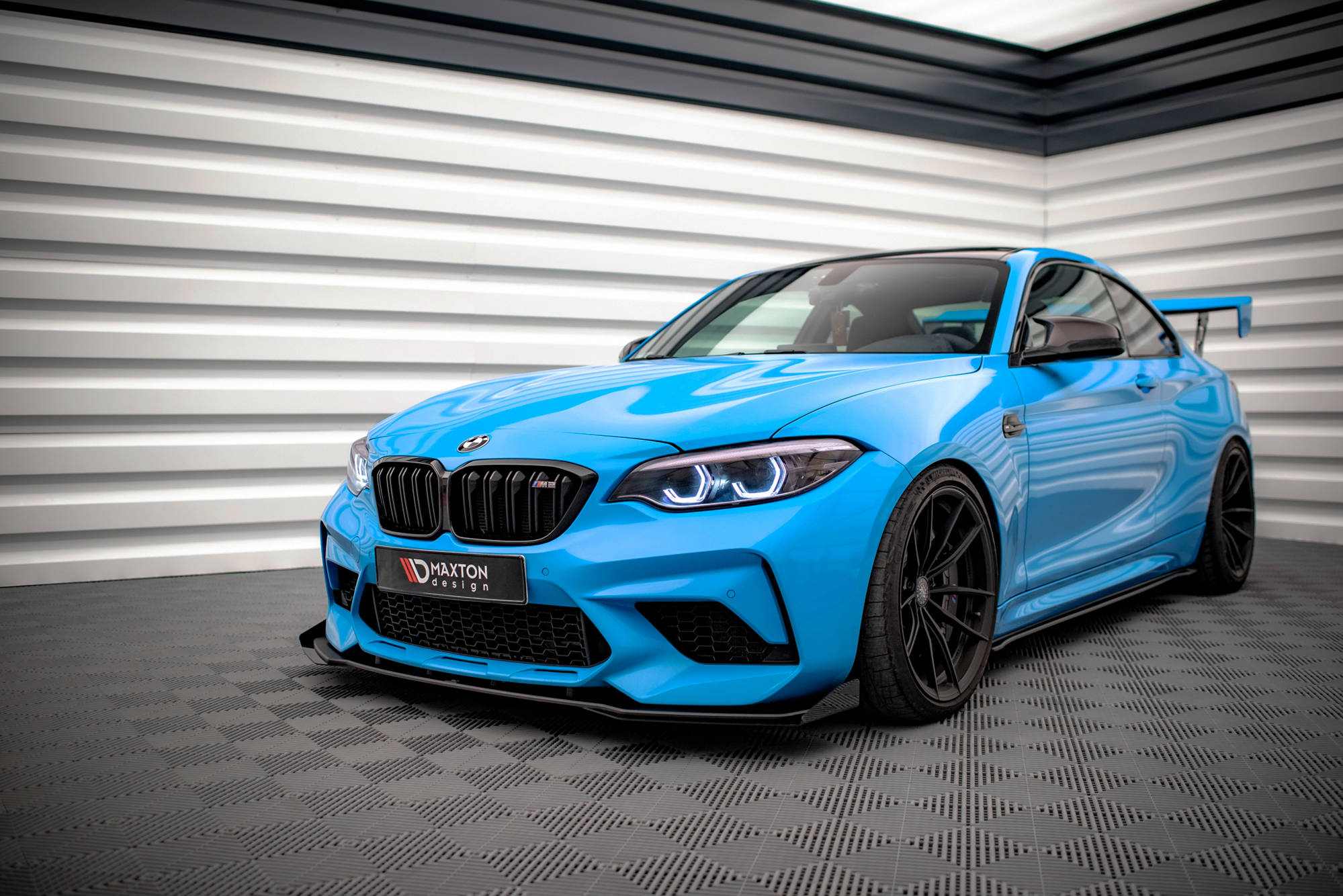 Spoiler på BMW M2 Competition F87 V.1 i lyseblått med svarte felger sett forfra fra venstre side.