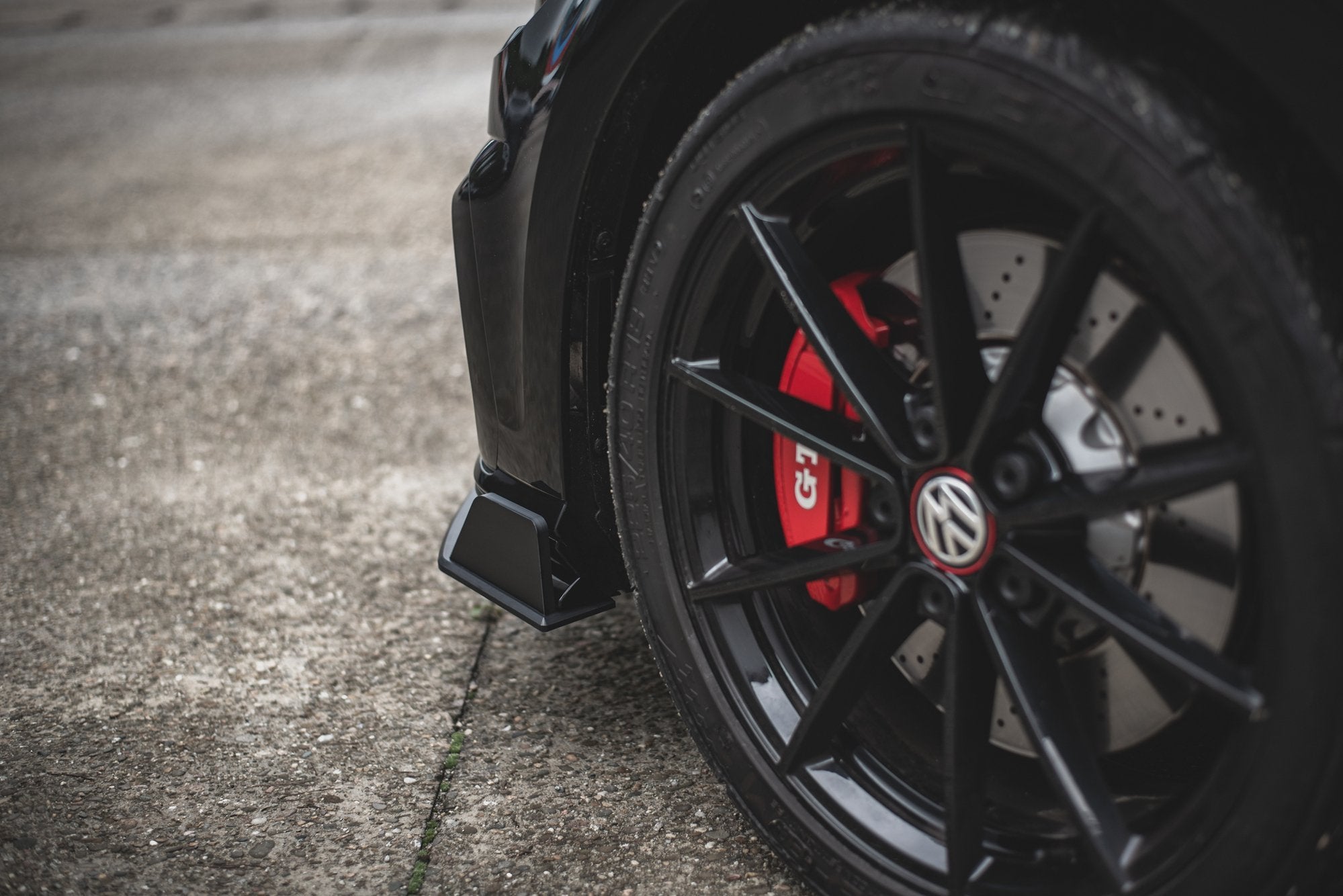 Spoiler på VW Golf 7 GTI Tcr viser sort aluminiumsfelg med rød bremsekaliper på asfalt.