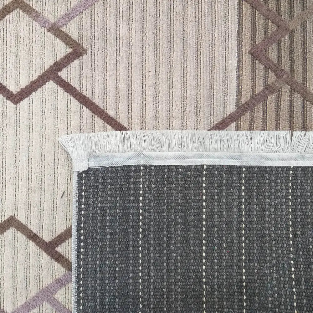 Tepe Moderne Hypnotik 06, nærbilde av hjørnet med lyst mønster, frynser og mørk bakside med lyse striper.