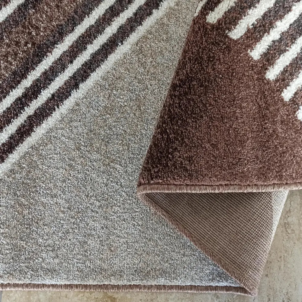 Tepe Otto teppe i brune og beige striper, nærbilde av brettet hjørne som viser baksiden og kantsømmen.